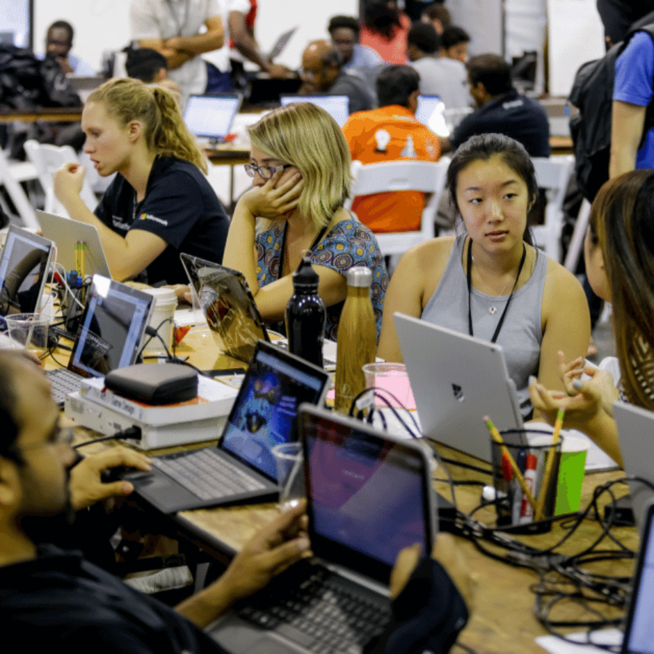 Cilvēki hakatlonā, sēžot pie galda un sarunājoties