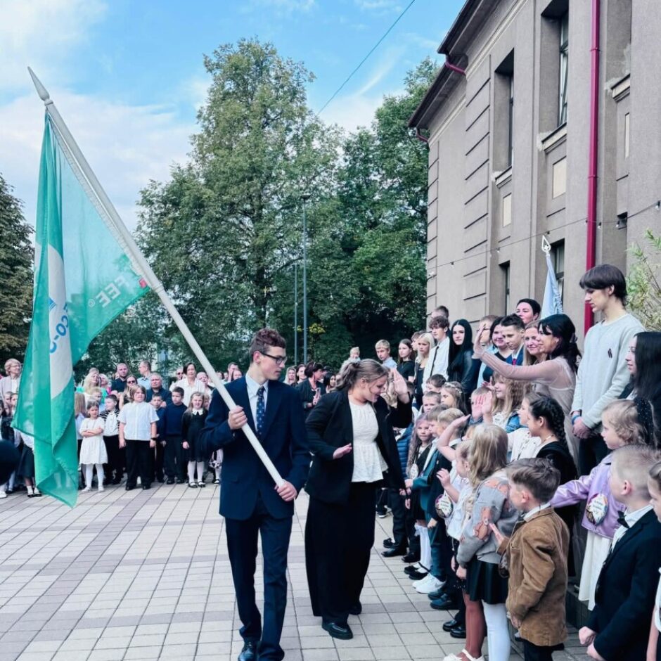 Jauns vīrietis uzvalkā nes tirkīzzilu karogu ar uzrakstu 